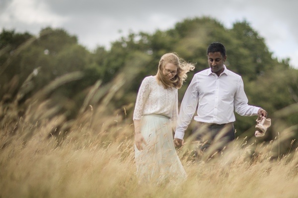 Ashley and Damon walk through long golden grass, holding hands. Damon carries Ashley's shoes as the wind tousles her blond locks and bends the grass.